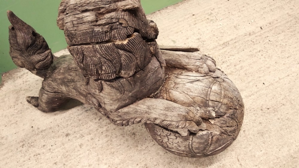 A weathered hand-carved wooden Chinese guardian lion resting its front paw on a decorative brocade ball. View IV