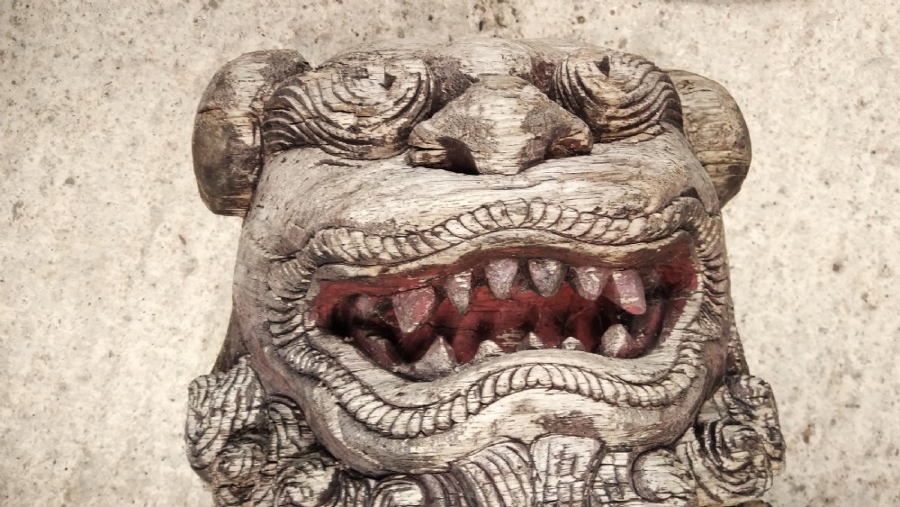 A weathered hand-carved wooden Chinese guardian lion resting its front paw on a decorative brocade ball. View V