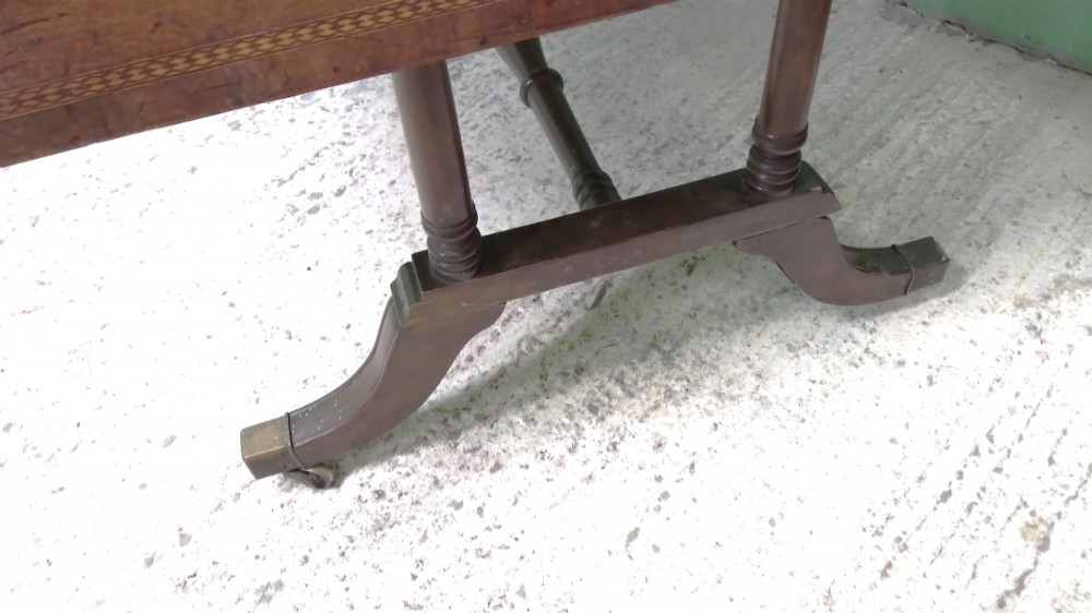 A George III mahogany drop-leaf sofa table featuring decorative border string inlay, two front drawers, a turned stretcher, and splayed legs fitted with brass castors. View IV