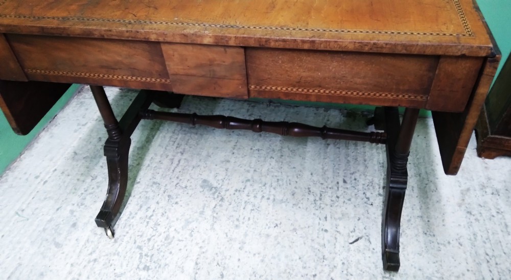 A George III mahogany drop-leaf sofa table featuring decorative border string inlay, two front drawers, a turned stretcher, and splayed legs fitted with brass castors. View V