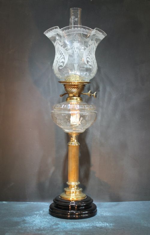 fig 1. An Art Nouveau oil lamp featuring a fluted brass column stem, clear etched glass shade with a ruffled rim, clear reservoir, and black base.