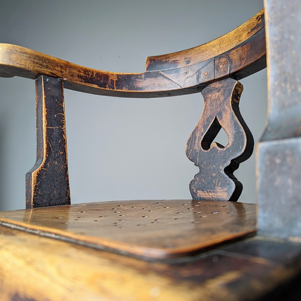 An antique dark wood childs barber chair featuring a swivel seat with a pierced pattern, curved arms, and a cast iron screw adjustment mechanism above splayed turned legs. View III