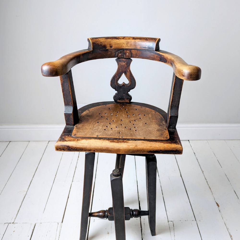 An antique dark wood childs barber chair featuring a swivel seat with a pierced pattern, curved arms, and a cast iron screw adjustment mechanism above splayed turned legs. View IV
