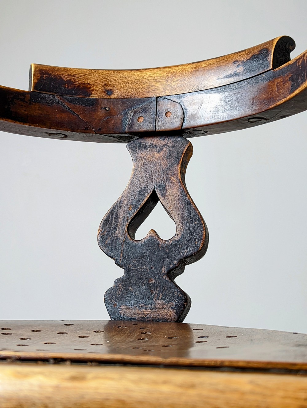 An antique dark wood childs barber chair featuring a swivel seat with a pierced pattern, curved arms, and a cast iron screw adjustment mechanism above splayed turned legs. View VII