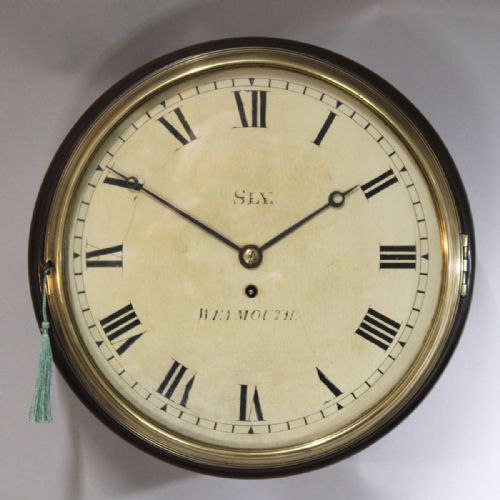 fig 1. A circular antique mahogany wall clock with a brass bezel, off-white dial displaying black Roman numerals, and maker signature Sly Weymouth.