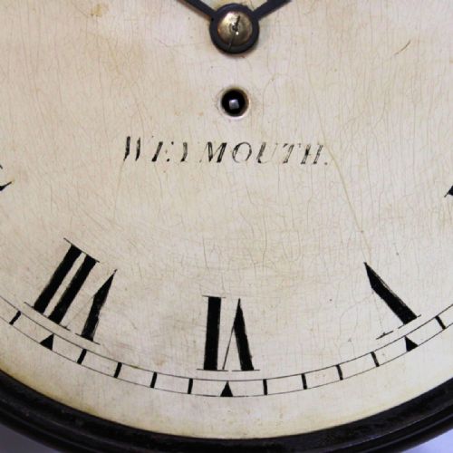 fig 4. A circular antique mahogany wall clock with a brass bezel, off-white dial displaying black Roman numerals, and maker signature Sly Weymouth.