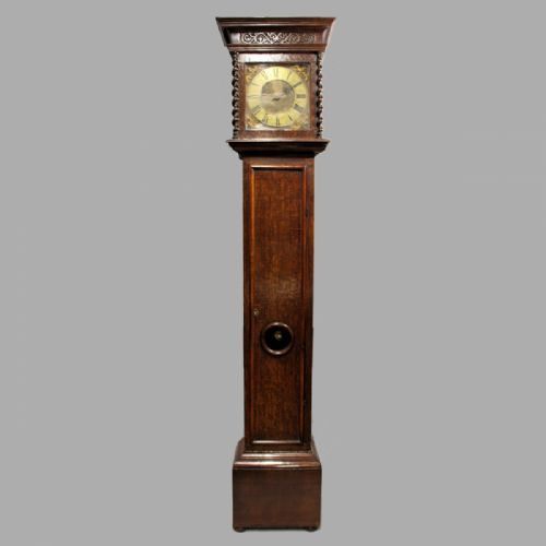 fig 2. A late 17th-century dark oak longcase clock hood featuring barley twist columns, carved frieze moulding, and a square brass dial.
