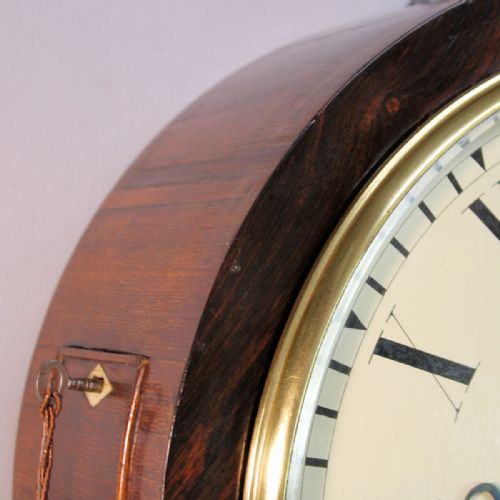 fig 1. A circular Victorian wall clock featuring a dark rosewood drum case, a polished brass bezel, and a cream painted dial signed L. Morris Islington with black Roman numerals.