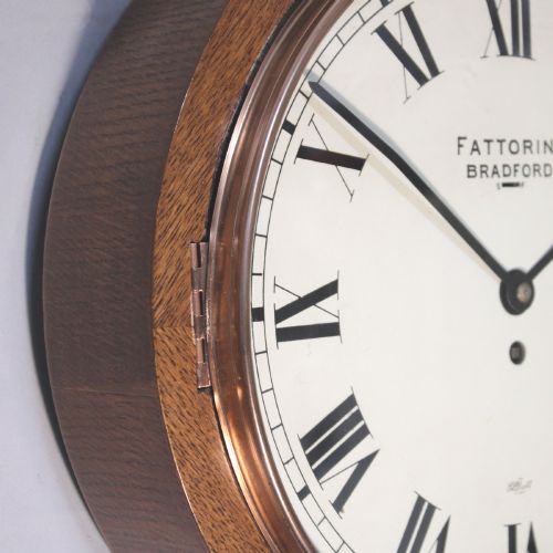 fig 1. A circular twentieth-century oak wall dial clock with black Roman numerals on a cream face, inscribed Fattorini Bradford.