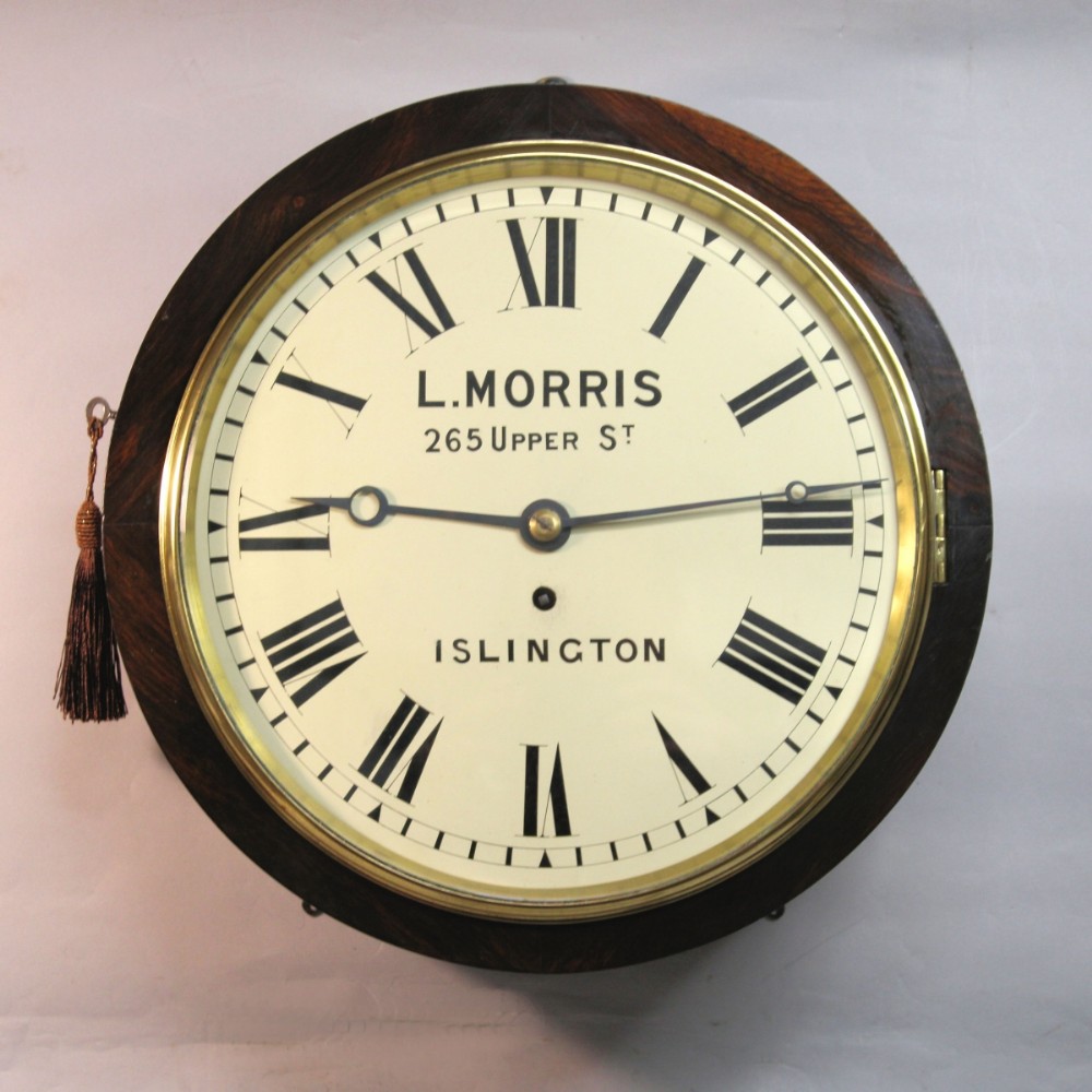 A circular Victorian wall clock featuring a dark rosewood drum case, a polished brass bezel, and a cream painted dial signed L. Morris Islington with black Roman numerals.