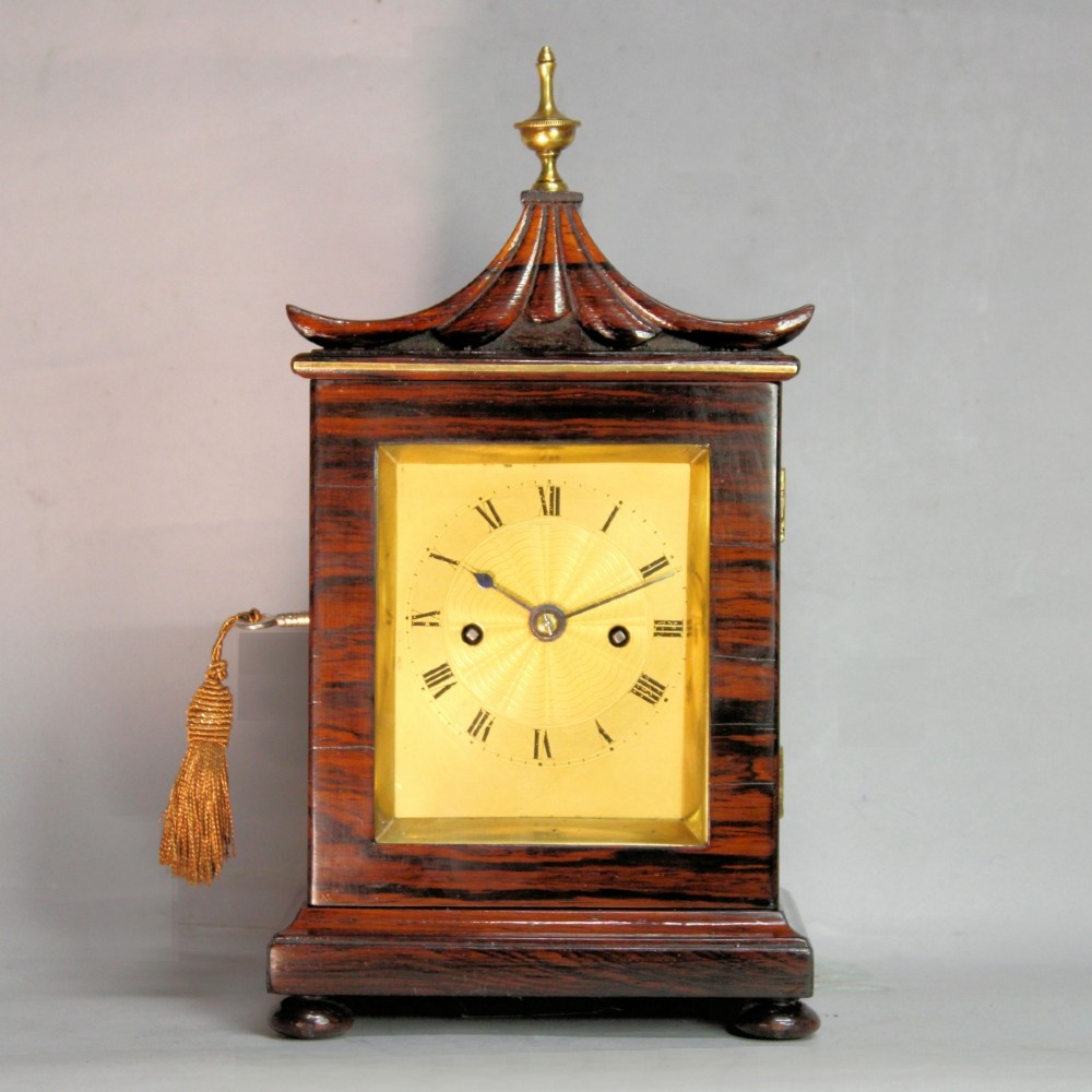A Victorian rosewood miniature bracket clock featuring a pagoda roof, brass finial, and engine-turned brass dial alongside a matching carved rosewood wall bracket. View II