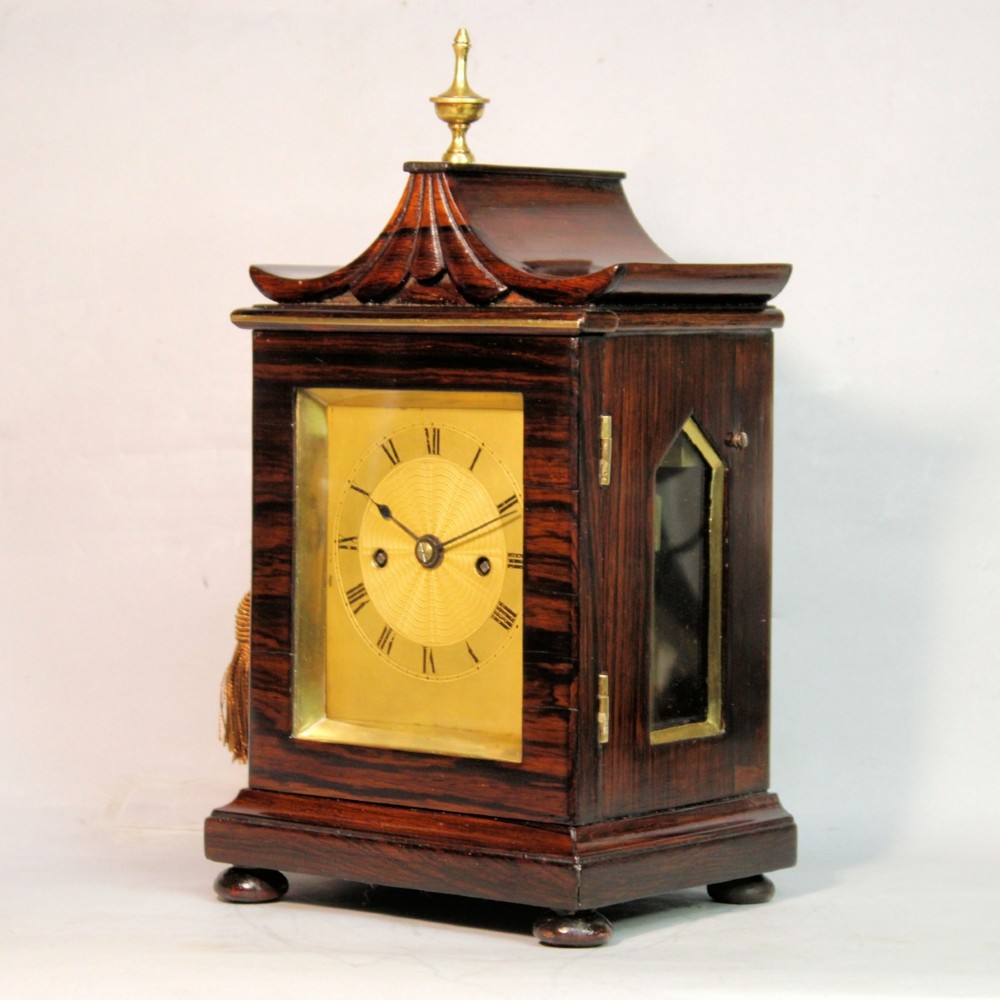 A Victorian rosewood miniature bracket clock featuring a pagoda roof, brass finial, and engine-turned brass dial alongside a matching carved rosewood wall bracket. View III