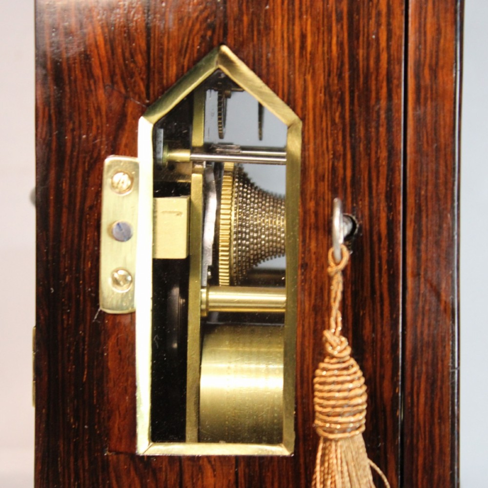 A Victorian rosewood miniature bracket clock featuring a pagoda roof, brass finial, and engine-turned brass dial alongside a matching carved rosewood wall bracket. View VII
