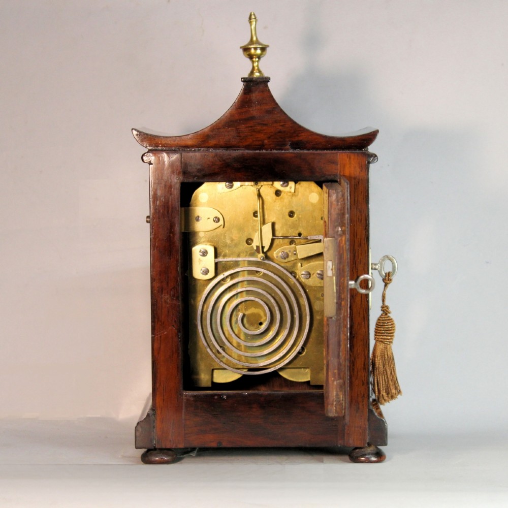 A Victorian rosewood miniature bracket clock featuring a pagoda roof, brass finial, and engine-turned brass dial alongside a matching carved rosewood wall bracket. View IX