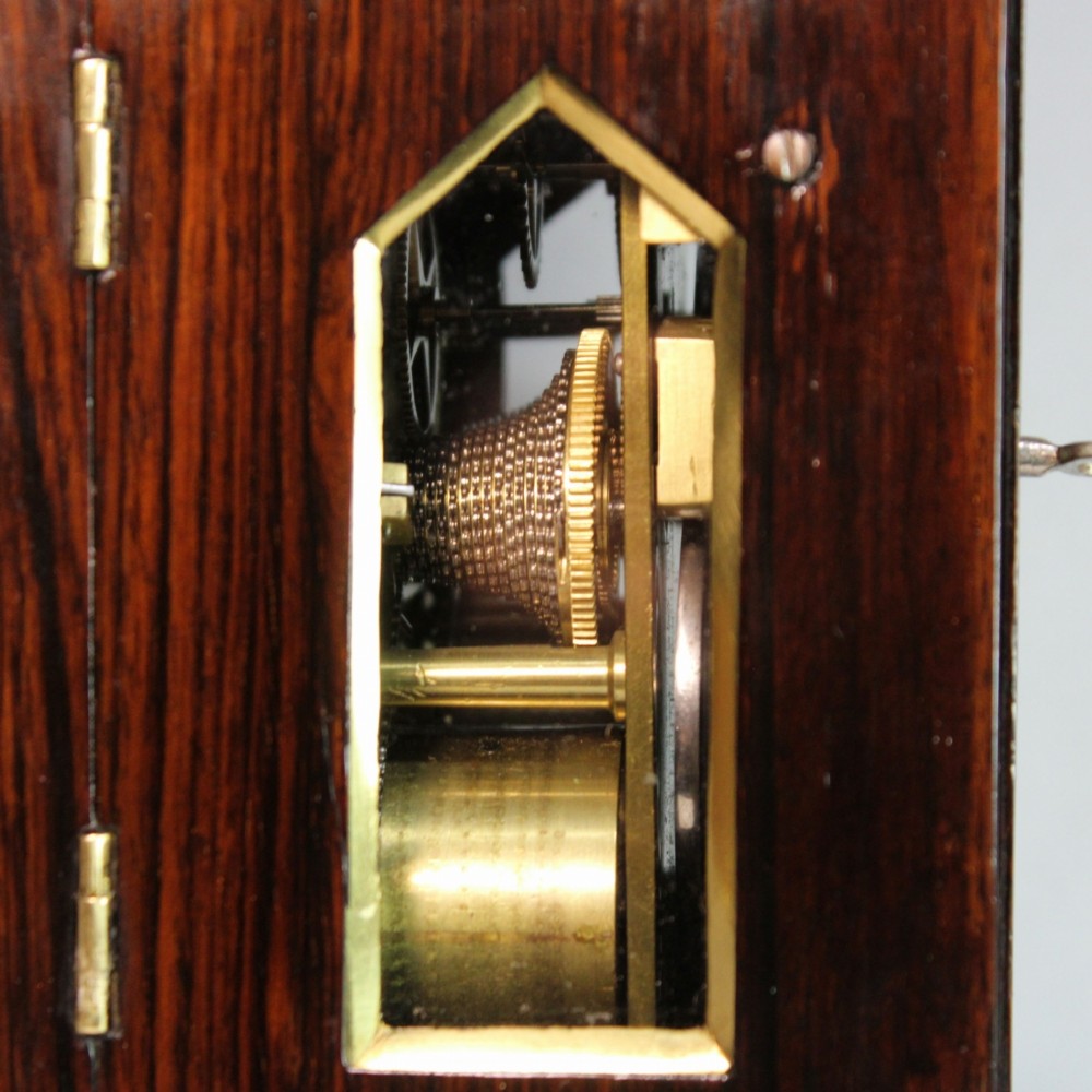 A Victorian rosewood miniature bracket clock featuring a pagoda roof, brass finial, and engine-turned brass dial alongside a matching carved rosewood wall bracket. View X