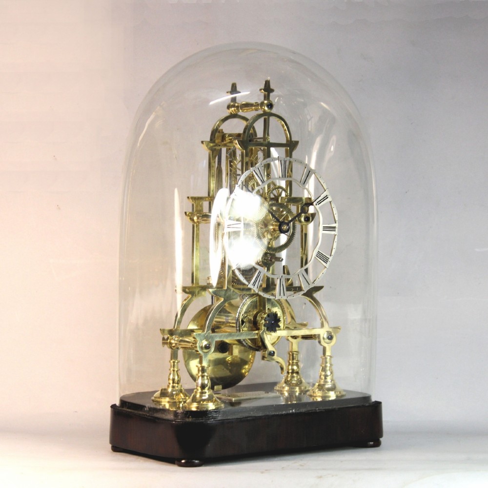 A Victorian brass skeleton clock featuring exposed internal gears, a silvered chapter ring, and a glass dome on a dark wooden base. View III