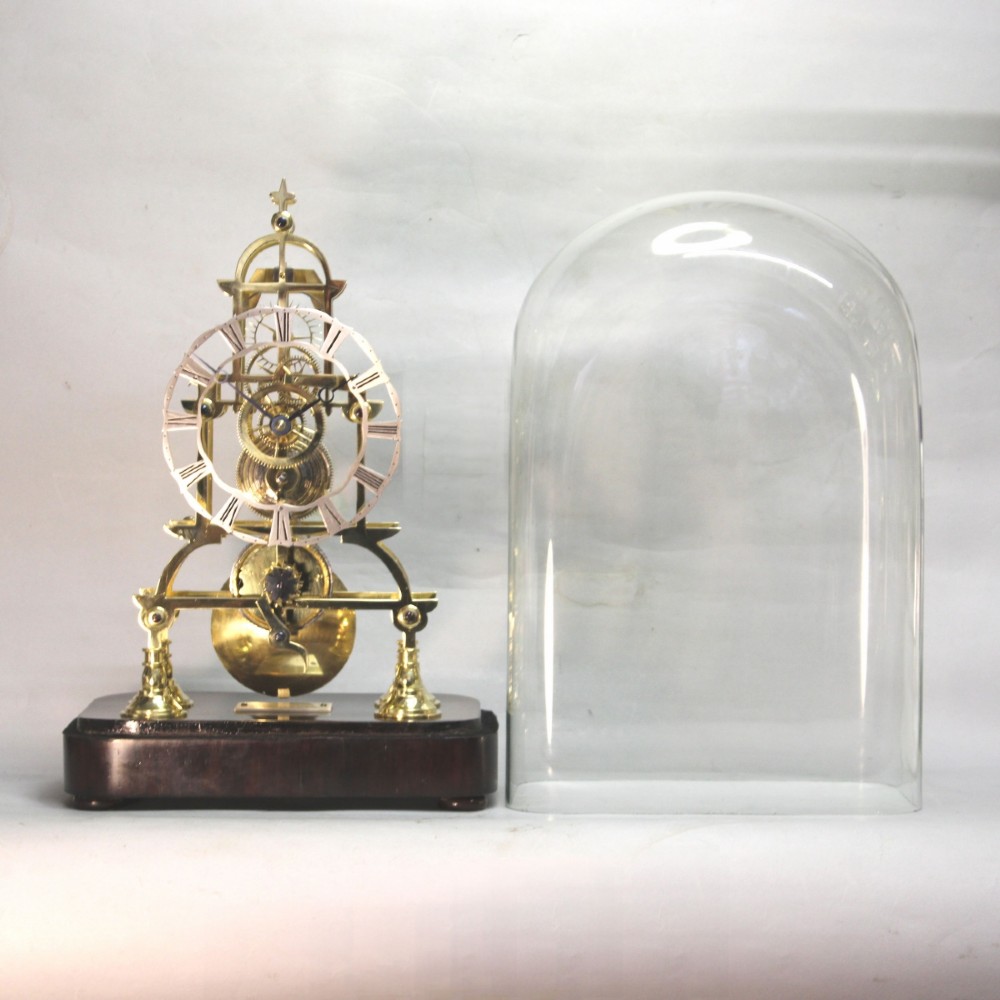 A Victorian brass skeleton clock featuring exposed internal gears, a silvered chapter ring, and a glass dome on a dark wooden base. View IV