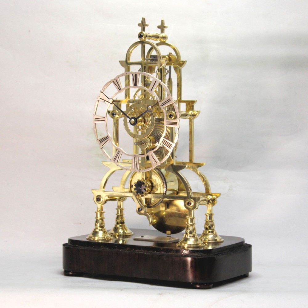 A Victorian brass skeleton clock featuring exposed internal gears, a silvered chapter ring, and a glass dome on a dark wooden base. View V