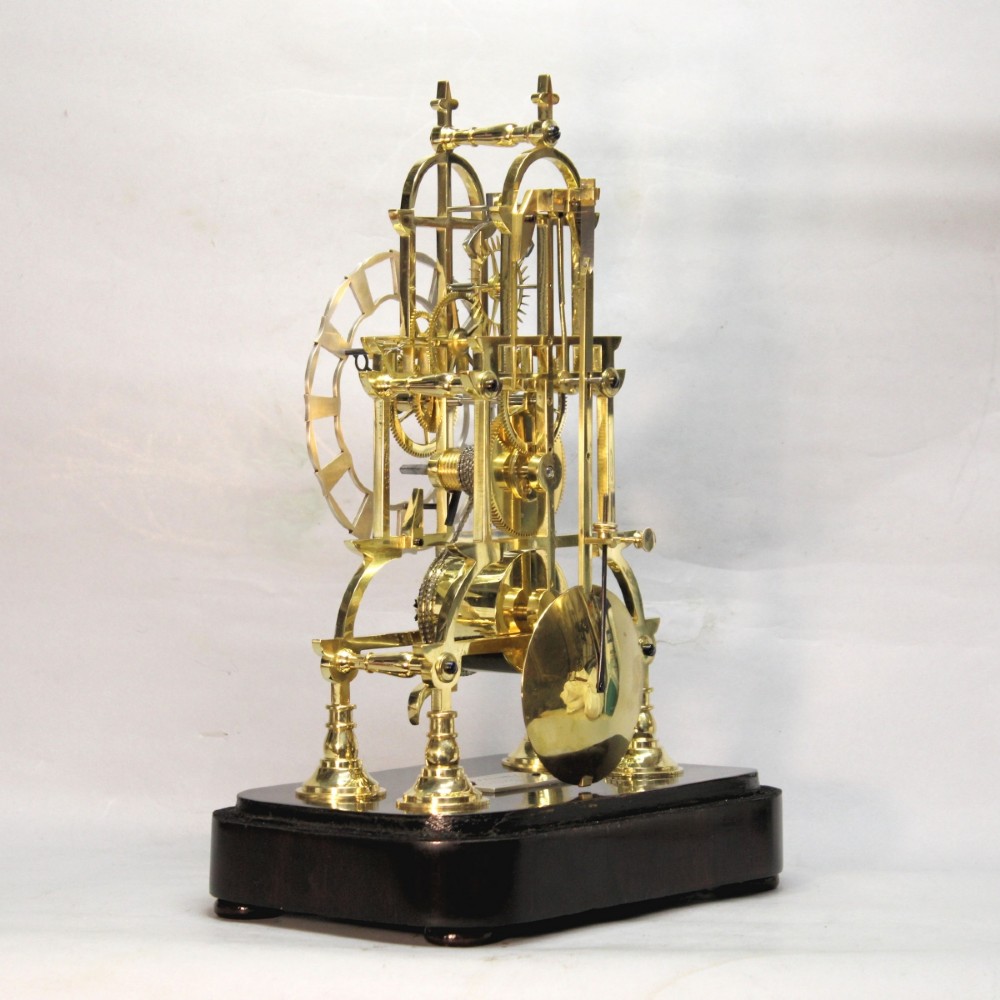 A Victorian brass skeleton clock featuring exposed internal gears, a silvered chapter ring, and a glass dome on a dark wooden base. View VII