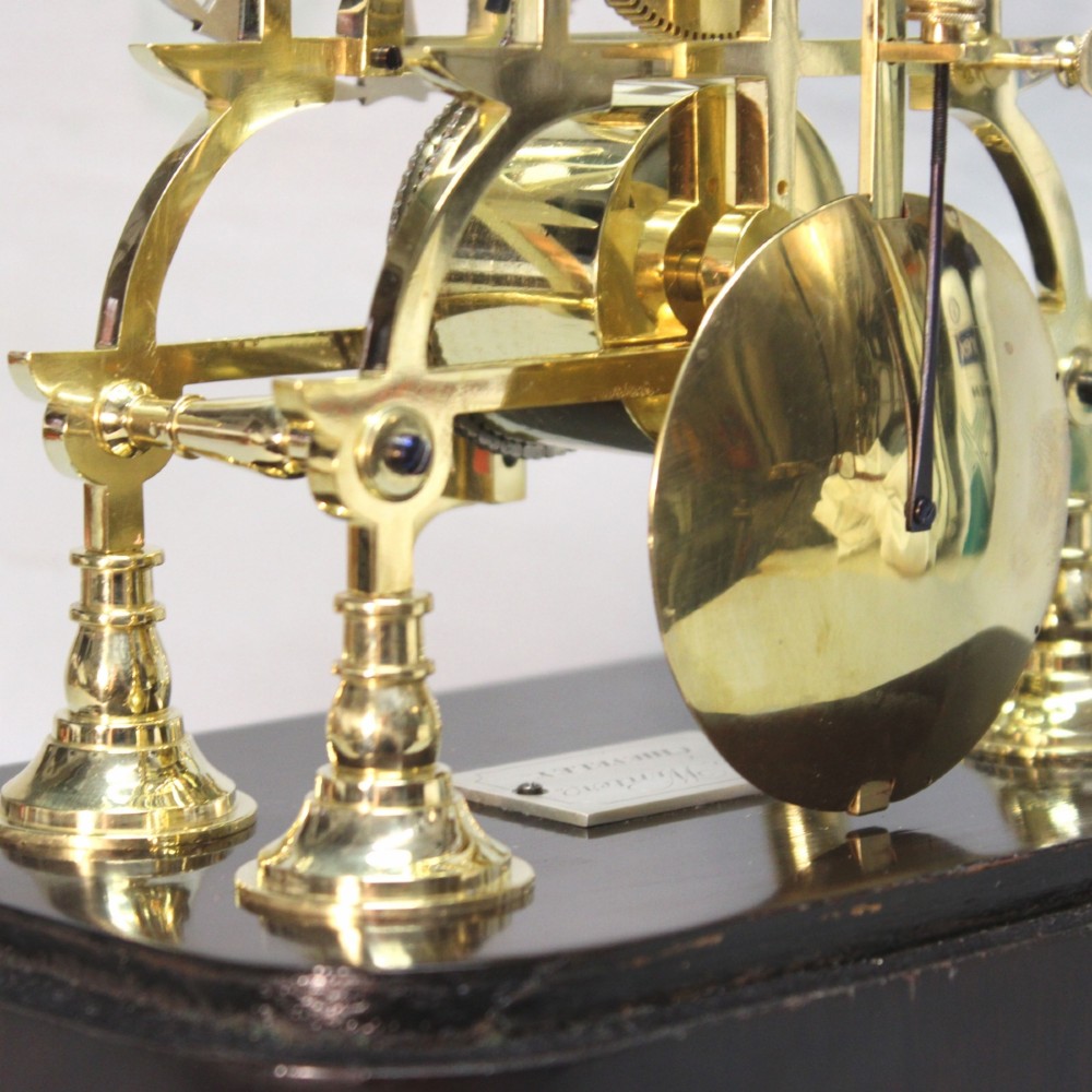 A Victorian brass skeleton clock featuring exposed internal gears, a silvered chapter ring, and a glass dome on a dark wooden base. View VIII