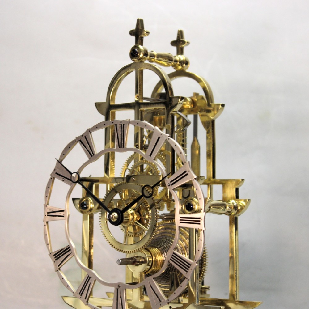 A Victorian brass skeleton clock featuring exposed internal gears, a silvered chapter ring, and a glass dome on a dark wooden base. View IX
