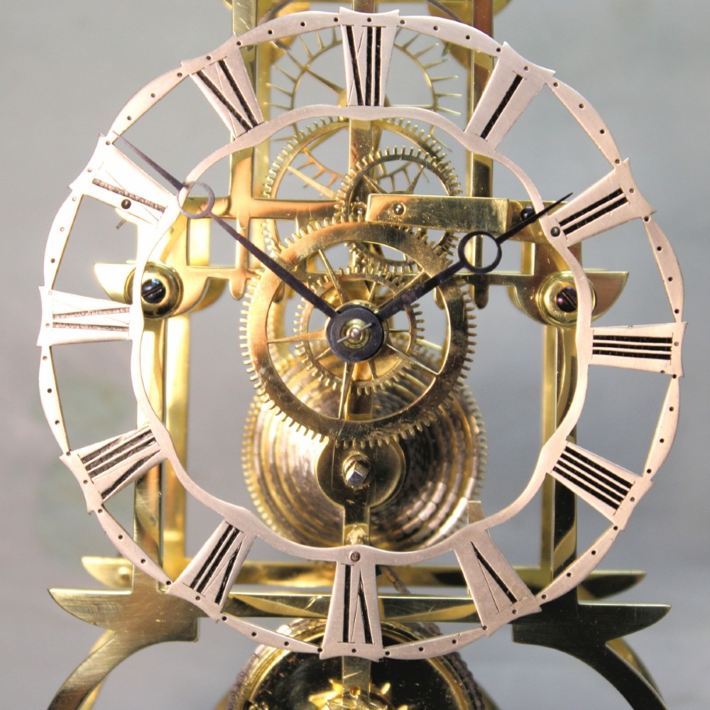 A Victorian brass skeleton clock featuring exposed internal gears, a silvered chapter ring, and a glass dome on a dark wooden base. View XII