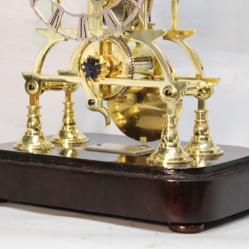 A Victorian brass skeleton clock featuring exposed internal gears, a silvered chapter ring, and a glass dome on a dark wooden base. View XIII