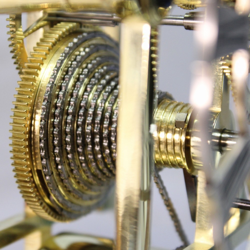 A Victorian brass skeleton clock featuring exposed internal gears, a silvered chapter ring, and a glass dome on a dark wooden base. View XV