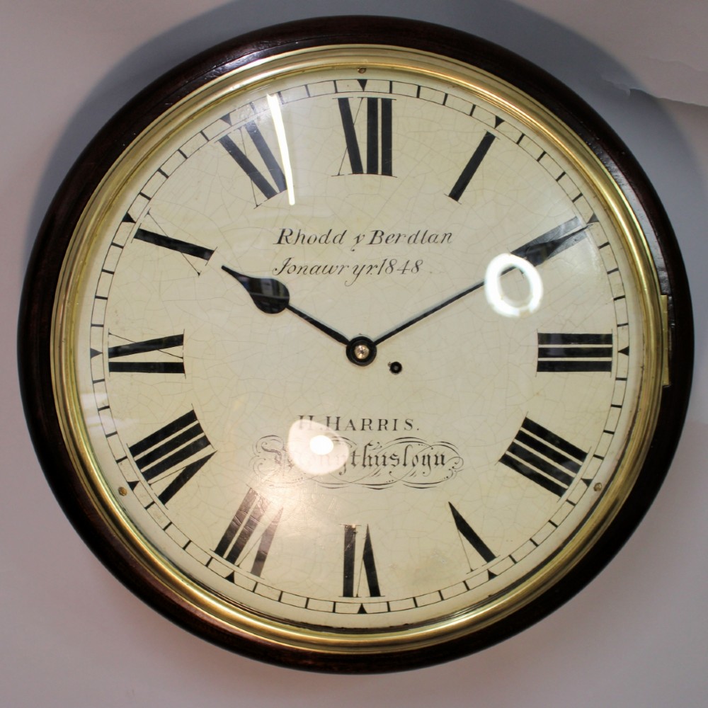 A circular Victorian wall clock featuring a dark mahogany surround, brass bezel, and cream painted dial with Roman numerals and black metal hands.