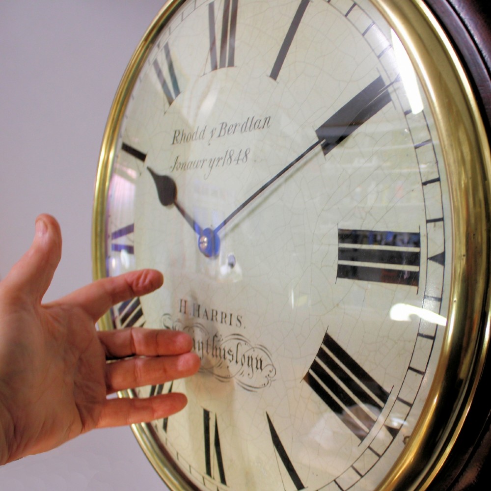 A circular Victorian wall clock featuring a dark mahogany surround, brass bezel, and cream painted dial with Roman numerals and black metal hands. View II