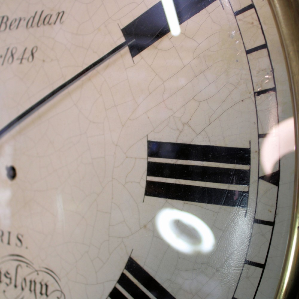 A circular Victorian wall clock featuring a dark mahogany surround, brass bezel, and cream painted dial with Roman numerals and black metal hands. View VII