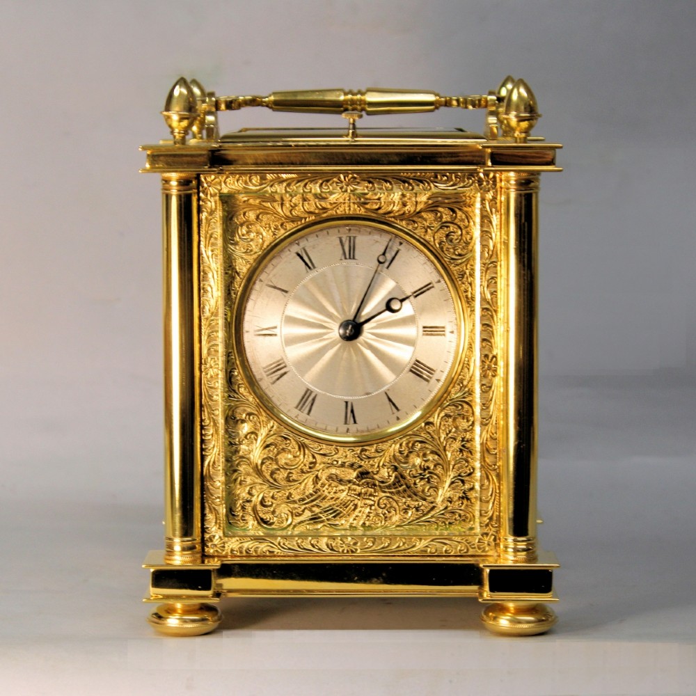 An ornate Victorian gilt brass carriage clock featuring detailed foliage engraving, corner columns, a decorative scroll handle, and a silvered sunburst dial with Roman numerals. View II