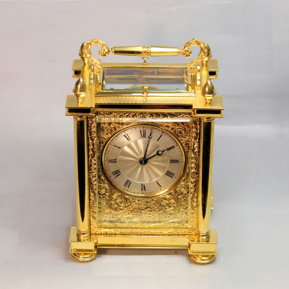 An ornate Victorian gilt brass carriage clock featuring detailed foliage engraving, corner columns, a decorative scroll handle, and a silvered sunburst dial with Roman numerals. View III