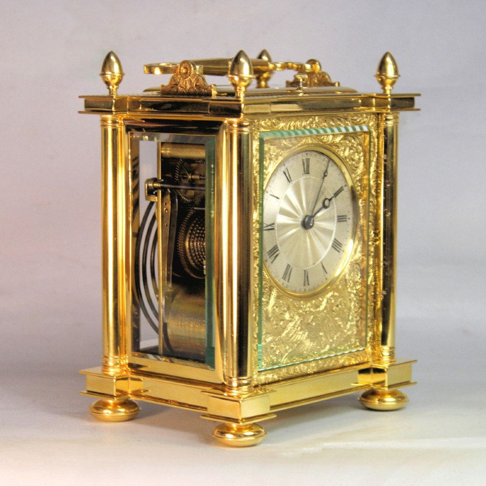 An ornate Victorian gilt brass carriage clock featuring detailed foliage engraving, corner columns, a decorative scroll handle, and a silvered sunburst dial with Roman numerals. View IV