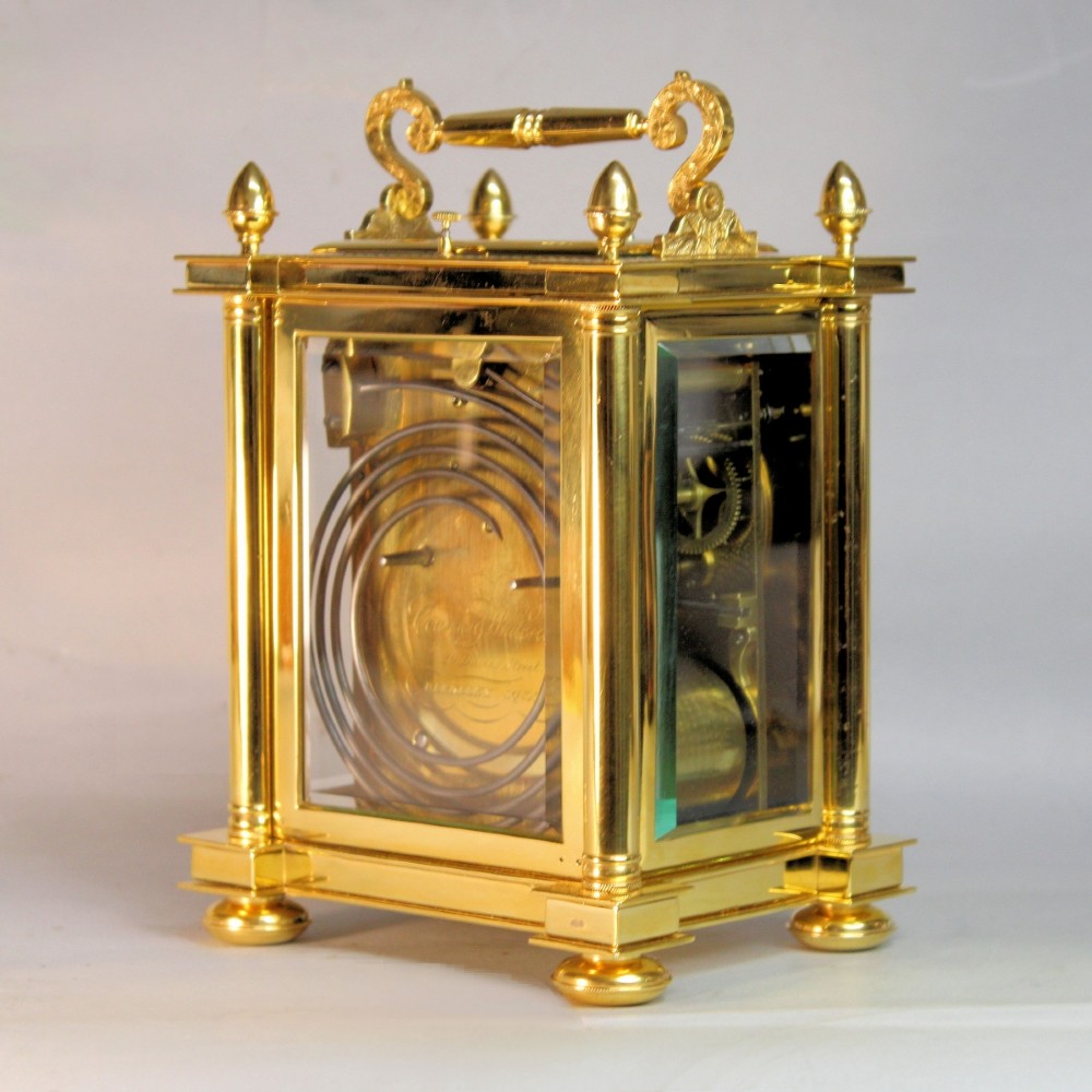 An ornate Victorian gilt brass carriage clock featuring detailed foliage engraving, corner columns, a decorative scroll handle, and a silvered sunburst dial with Roman numerals. View VI