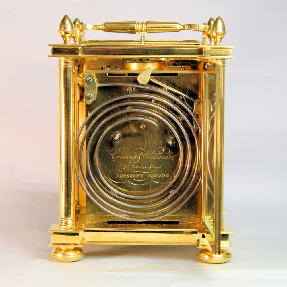 An ornate Victorian gilt brass carriage clock featuring detailed foliage engraving, corner columns, a decorative scroll handle, and a silvered sunburst dial with Roman numerals. View VII