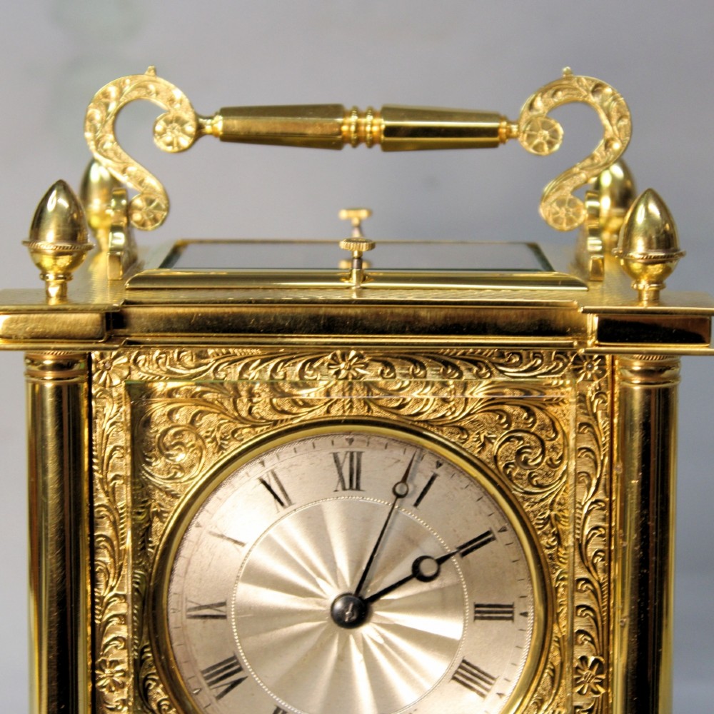 An ornate Victorian gilt brass carriage clock featuring detailed foliage engraving, corner columns, a decorative scroll handle, and a silvered sunburst dial with Roman numerals. View VIII