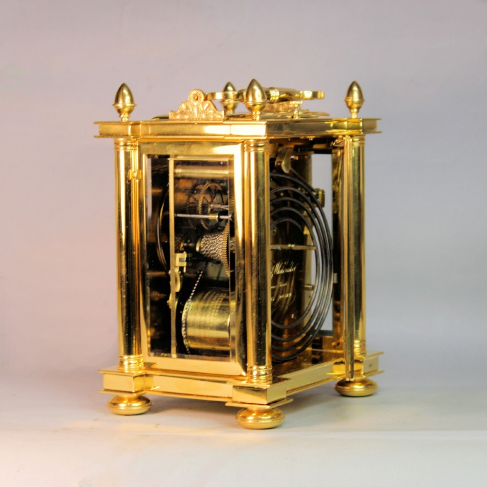 An ornate Victorian gilt brass carriage clock featuring detailed foliage engraving, corner columns, a decorative scroll handle, and a silvered sunburst dial with Roman numerals. View IX