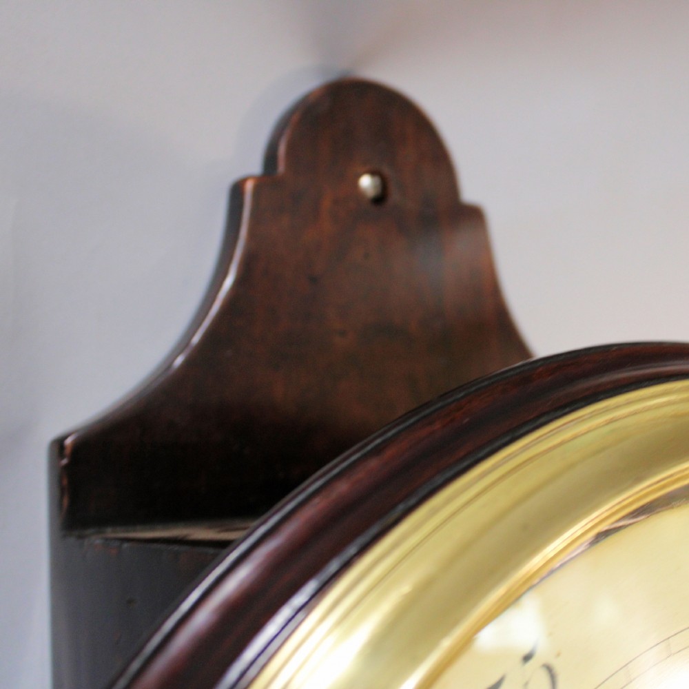A late 18th-century Georgian mahogany wall clock featuring a circular cream painted dial with Roman numerals, a brass bezel, and a salt-box wooden case. View XI