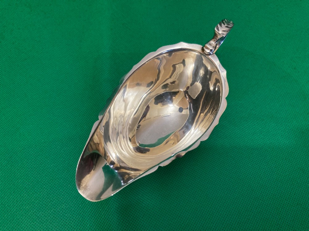 A polished silver sauce boat featuring a shaped rim, a scroll handle, and three pad feet. View III