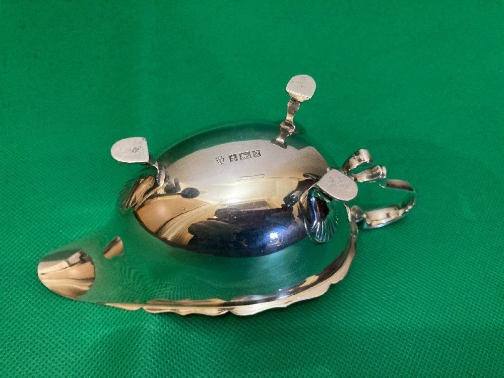 A polished silver sauce boat featuring a shaped rim, a scroll handle, and three pad feet. View IV