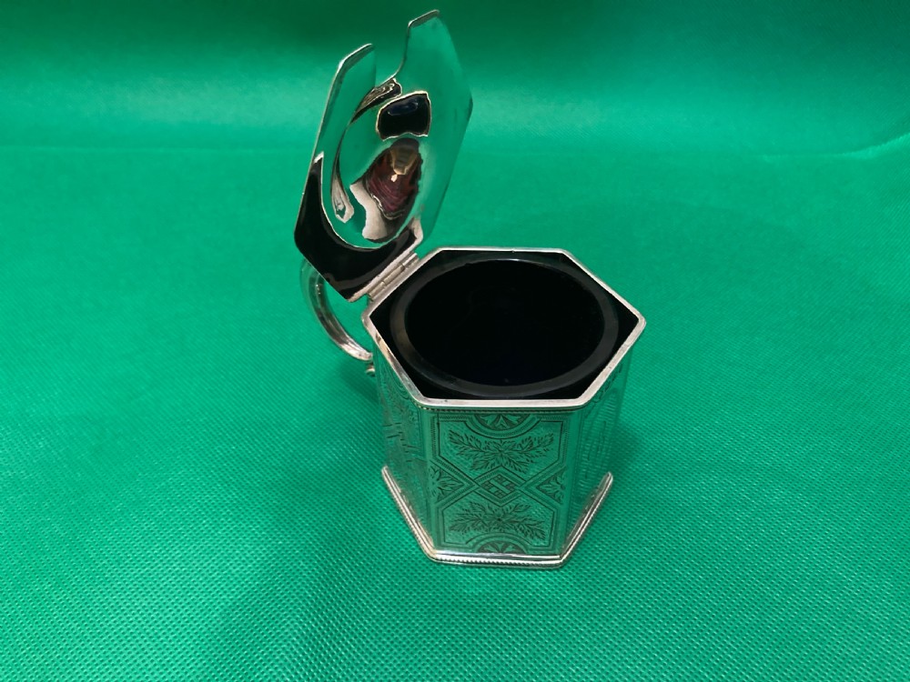 A Victorian-style hexagonal silver mustard pot with bright-cut foliate engraving, a shell thumbpiece, a curved handle, and a blue glass liner. View IV