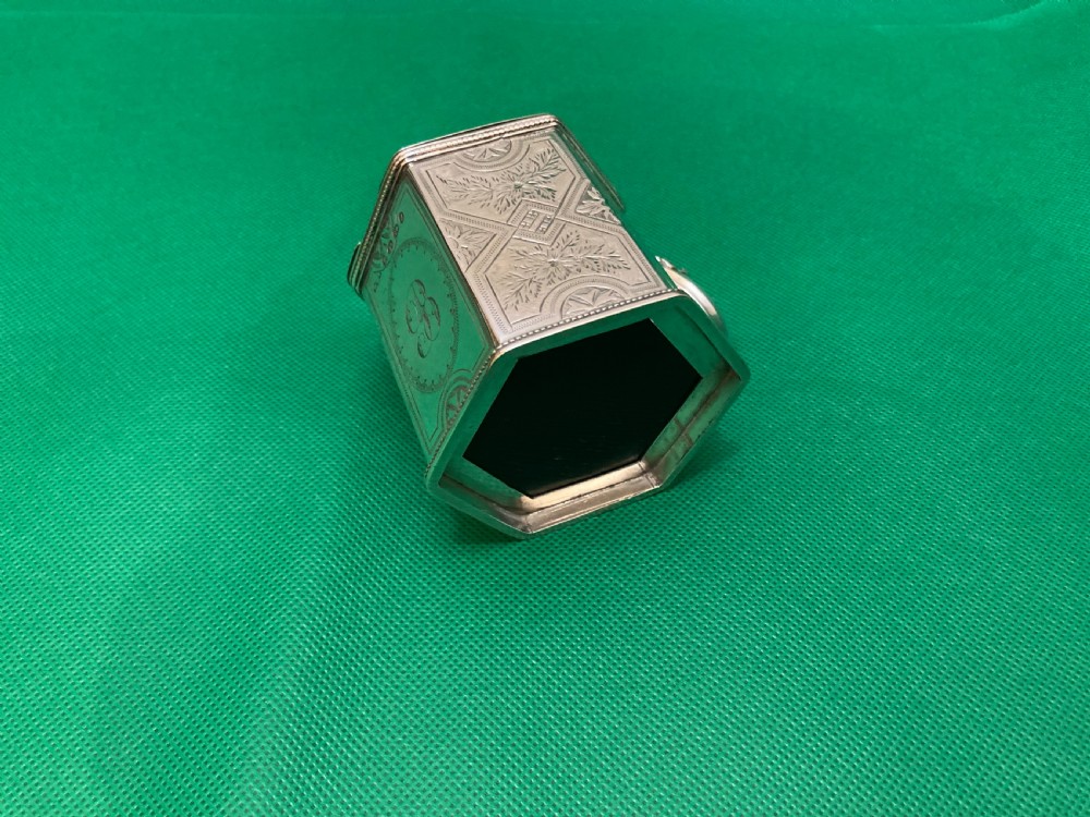 A Victorian-style hexagonal silver mustard pot with bright-cut foliate engraving, a shell thumbpiece, a curved handle, and a blue glass liner. View V