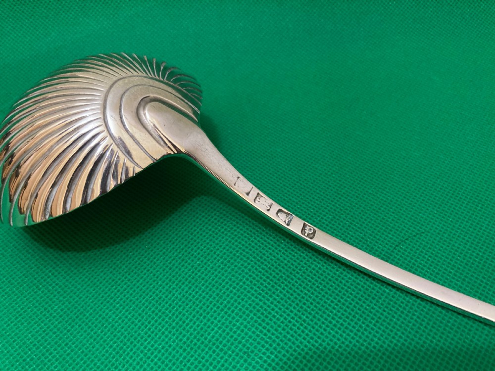 An antique silver punch ladle featuring a deeply fluted shell-shaped bowl and a curved handle with an engraved crest at the terminal. View III