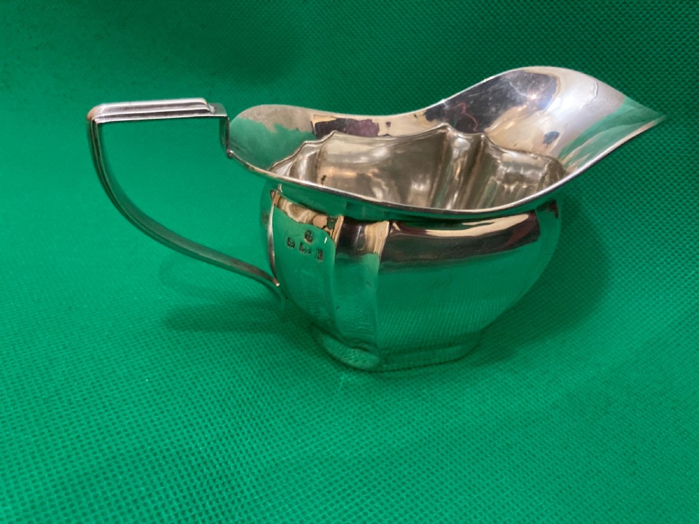 A sterling silver cream jug with a panelled body, an angular geometric handle, and visible hallmarks stamped on the exterior side.
