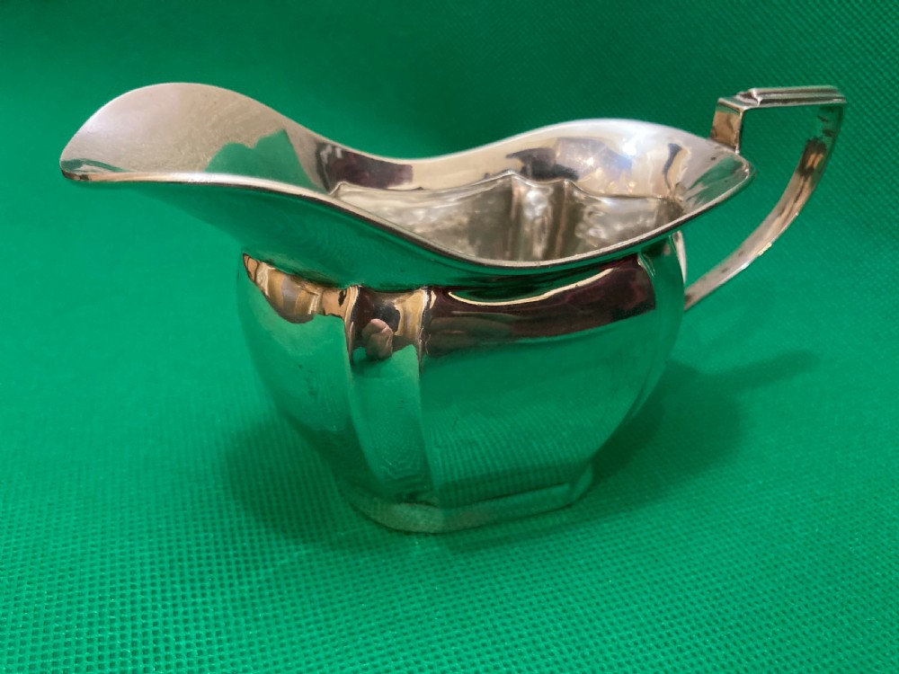 A sterling silver cream jug with a panelled body, an angular geometric handle, and visible hallmarks stamped on the exterior side. View II
