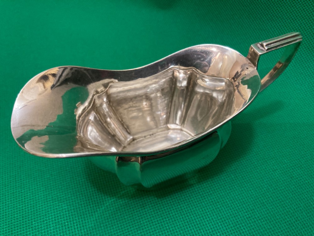 A sterling silver cream jug with a panelled body, an angular geometric handle, and visible hallmarks stamped on the exterior side. View III