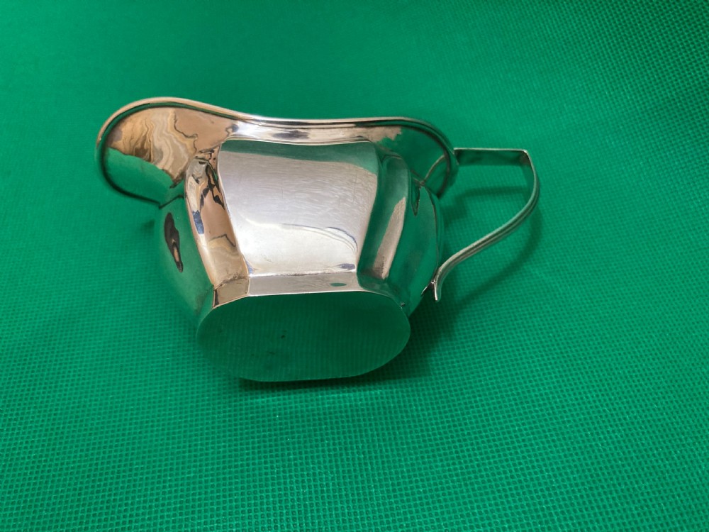 A sterling silver cream jug with a panelled body, an angular geometric handle, and visible hallmarks stamped on the exterior side. View IV