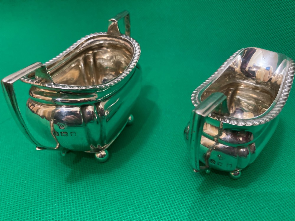 A matching silver cream jug and two-handled sugar bowl featuring gadrooned rims, angular handles, and small ball feet. View IV