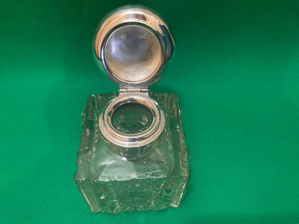 A square clear cut glass inkwell with a diamond facet pattern and a polished silver hinged domed cap. View II
